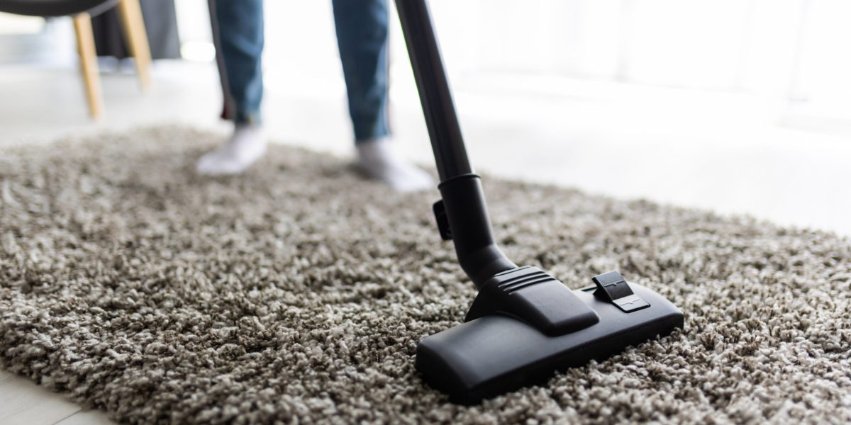 Close up of woman with legs vacuum cleaner cleaning carpet at home